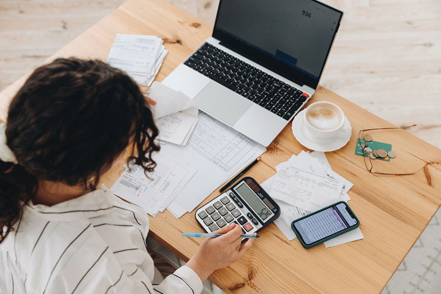 © Sheremetio - stock.adobe.com Foto: Frau tippt auf Taschenrechner mit Laptop am Arbeitstisch